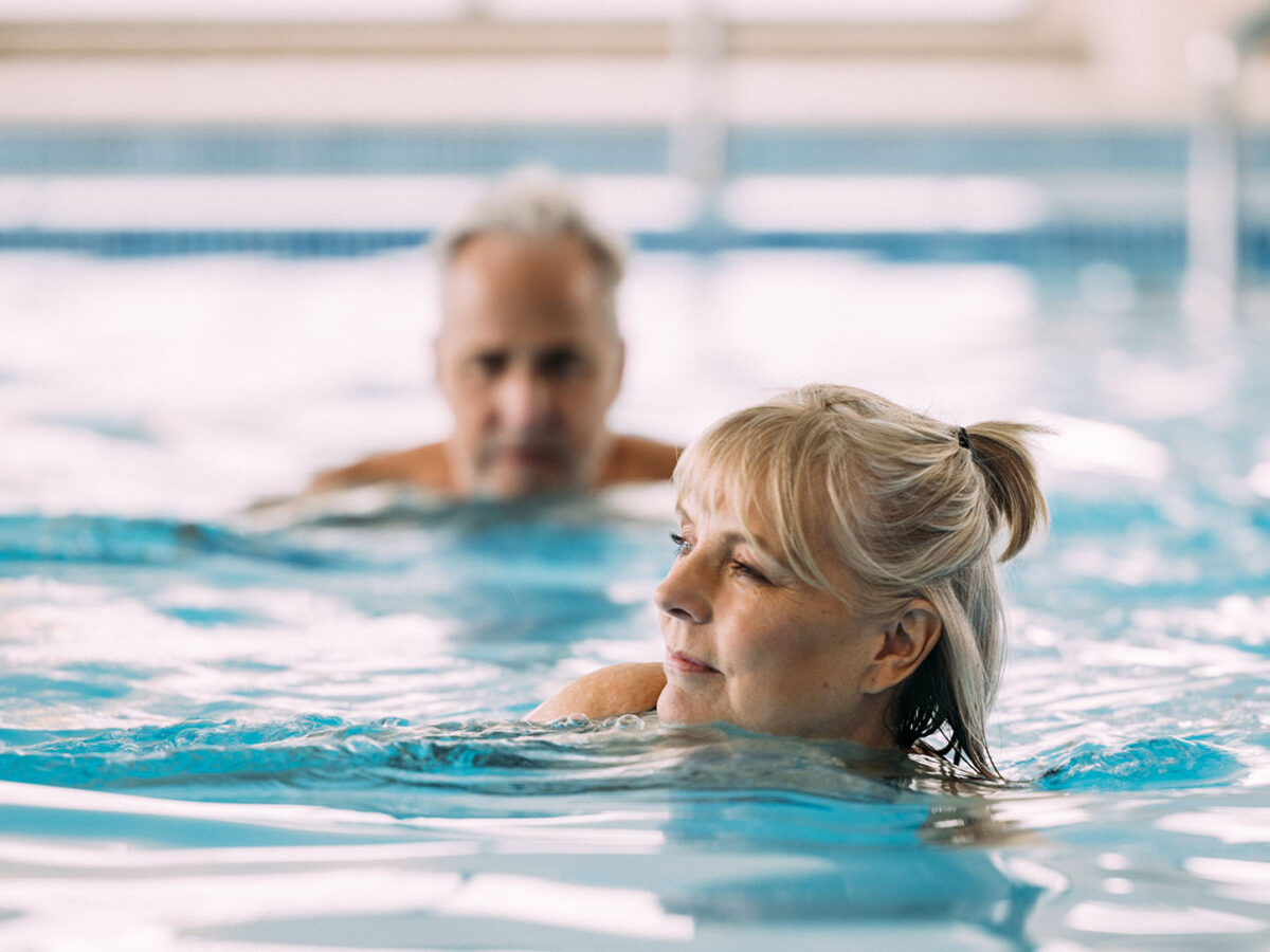 Older couple gently swimming in an indoor heated swimming pool