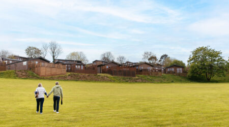 Couple walking in a grassed field below holiday homes