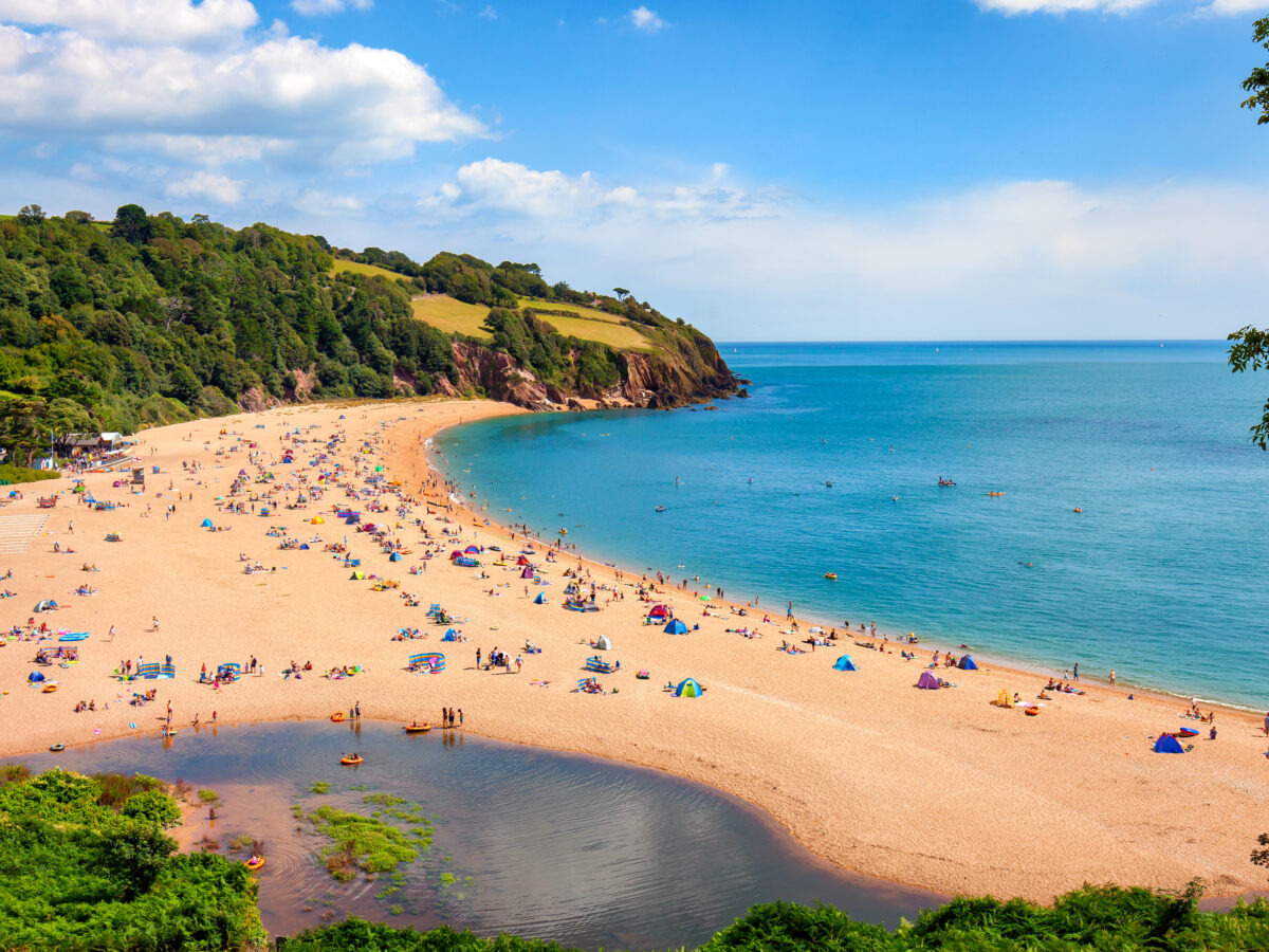 A sandy beach with a bay, bright blue waters, and holiday makers making the most of the sunshine.