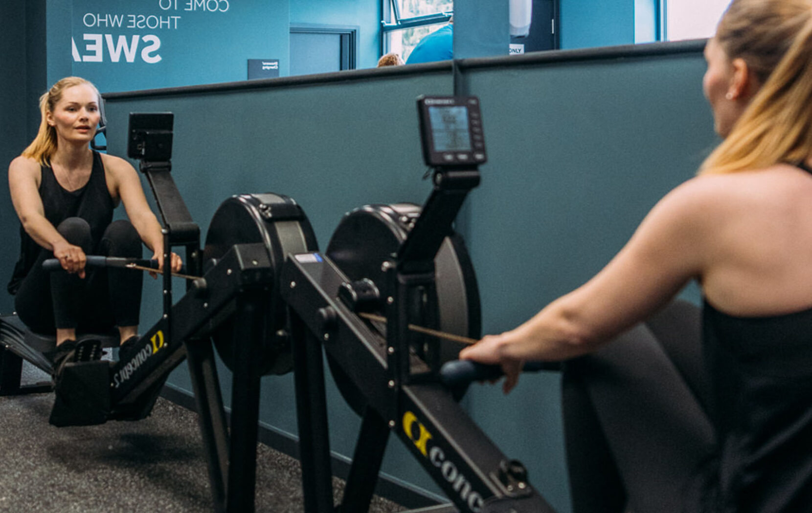 Woman exercising on the row machine, while seeing herself in the mirror