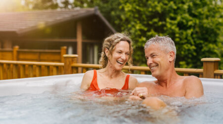 Couple laughing in a steaming bublly hot tub with trees and wooden balcony behind them